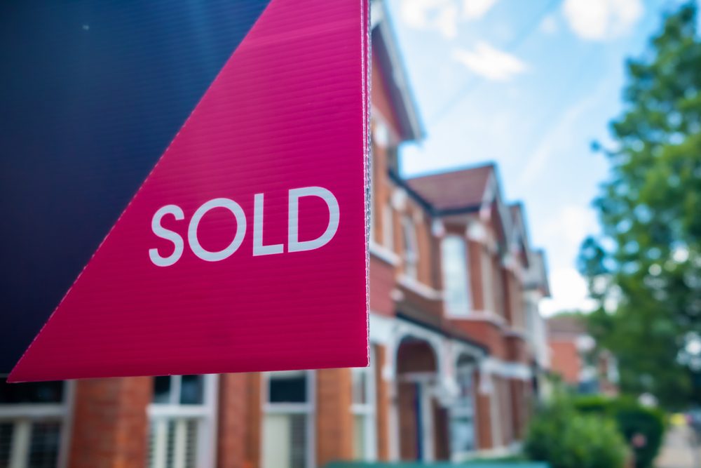 Estate agent sold sign with defocussed street of houses in background
